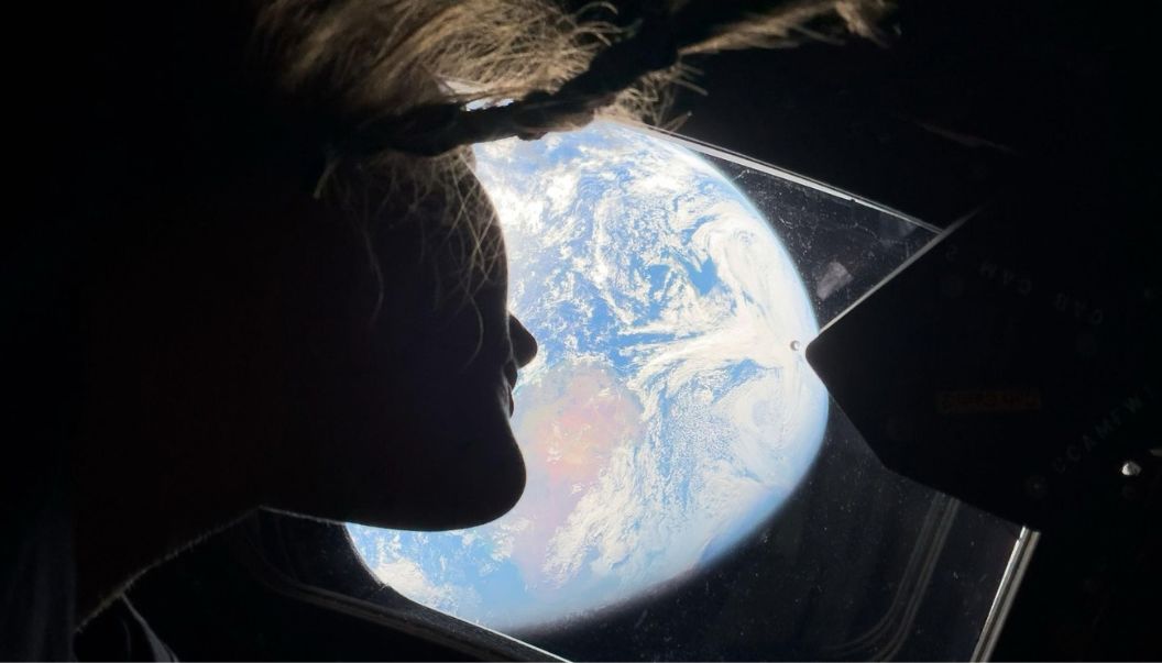 Christina Koch looking out at Earth from the Orion spacecraft during the Artemis II mission with her braided hair floating in zero gravity