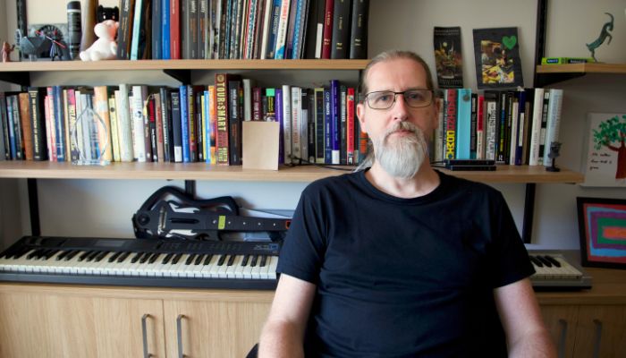 Steve Collins sitting in his office with shelf of books and trinkets behind him